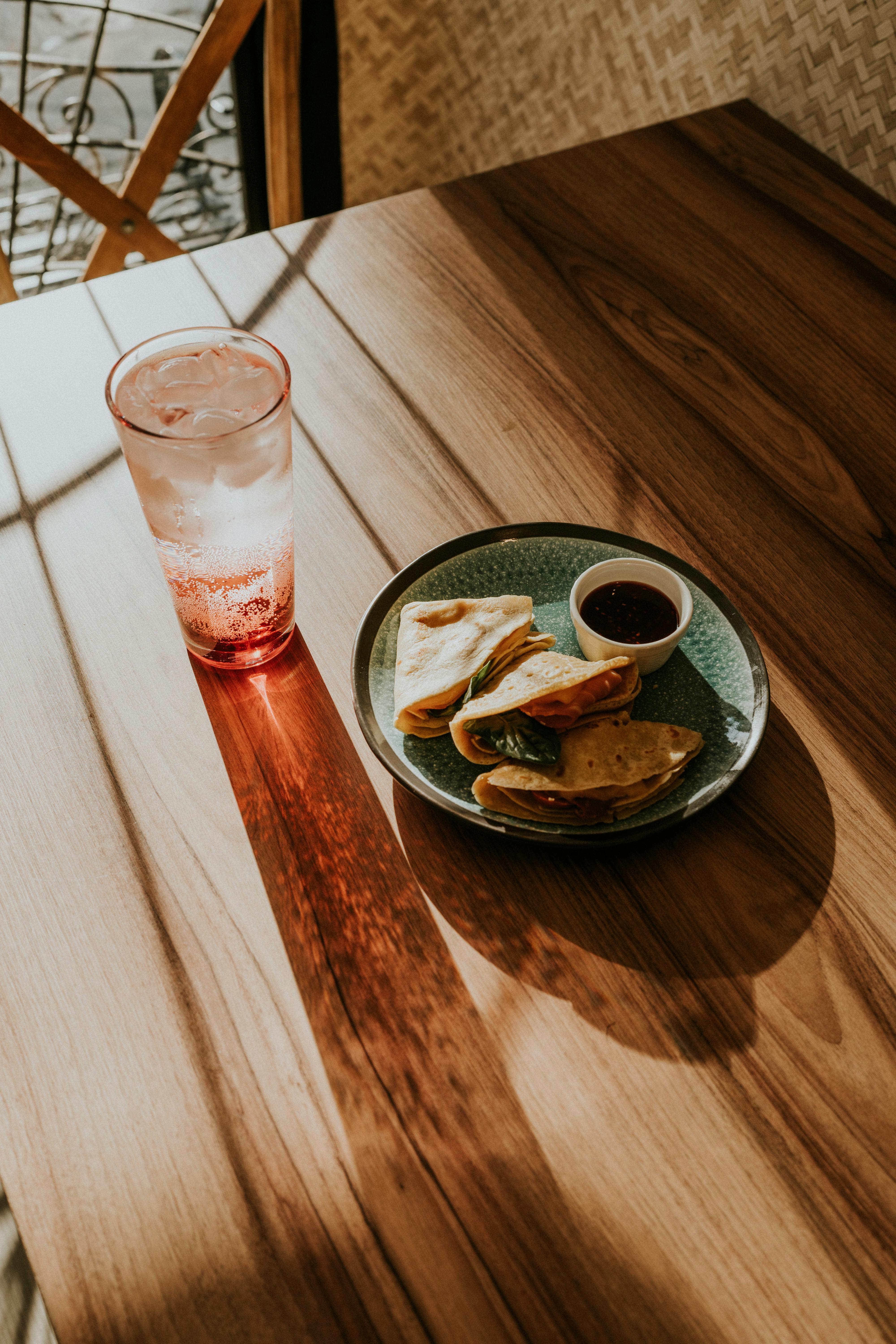 A plate of tortillas and cold drink on a sunlit wooden table, perfect for a cozy café setting.