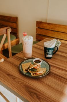 A warm cafe scene featuring a frothy milkshake, coffee mug, and plate of crepes on a wooden table.