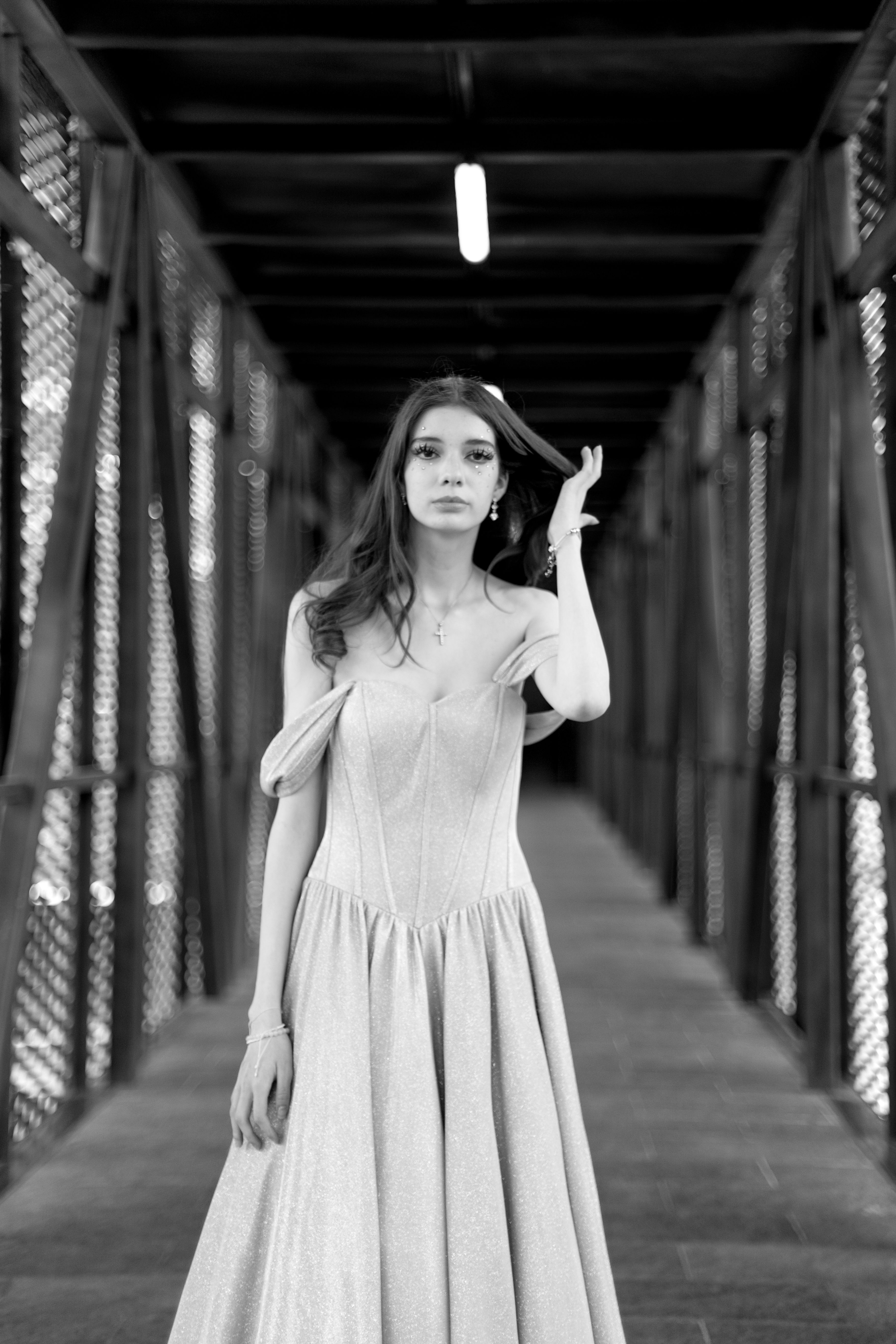 Black and white portrait of a woman in a flowing dress on a pedestrian bridge.