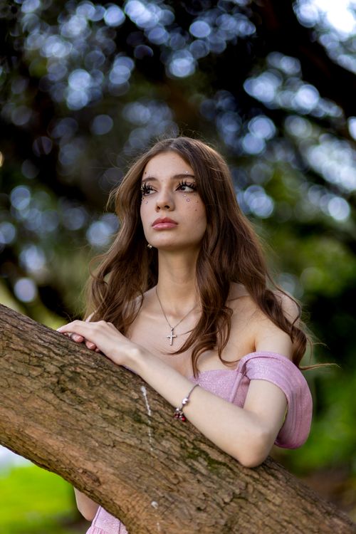 A woman in a pink dress leaning against a tree · Free Stock Photo