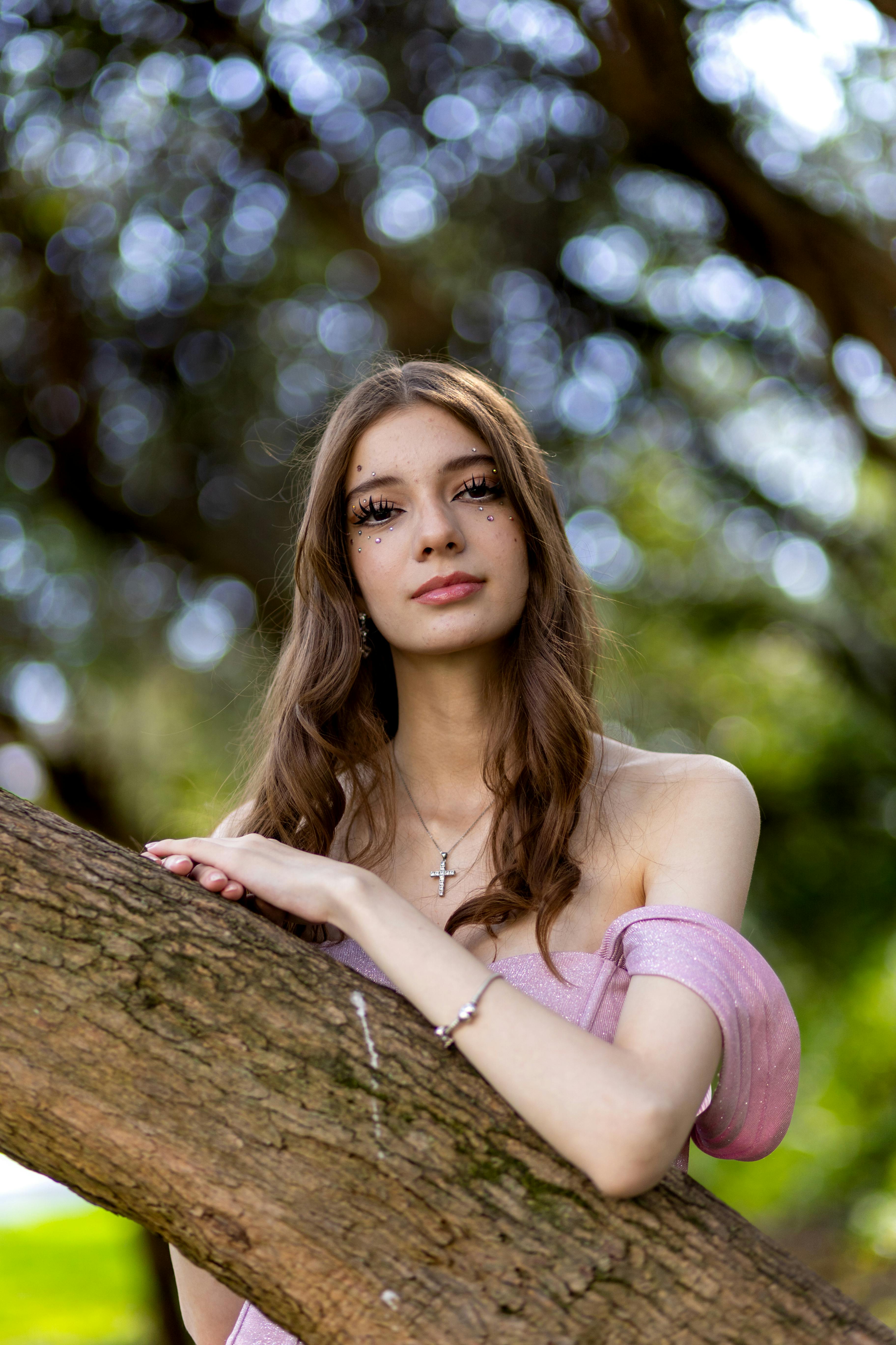 a beautiful young woman in a pink dress leaning against a tree