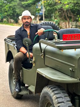 A man in a vintage jeep wearing a fedora enjoys an off-road adventure on a rural road.