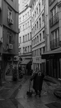 A lone pedestrian walks through rainy urban alleyways lined with tall buildings.