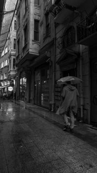 Black and white photo of a rainy city street, capturing a pedestrian with an umbrella.