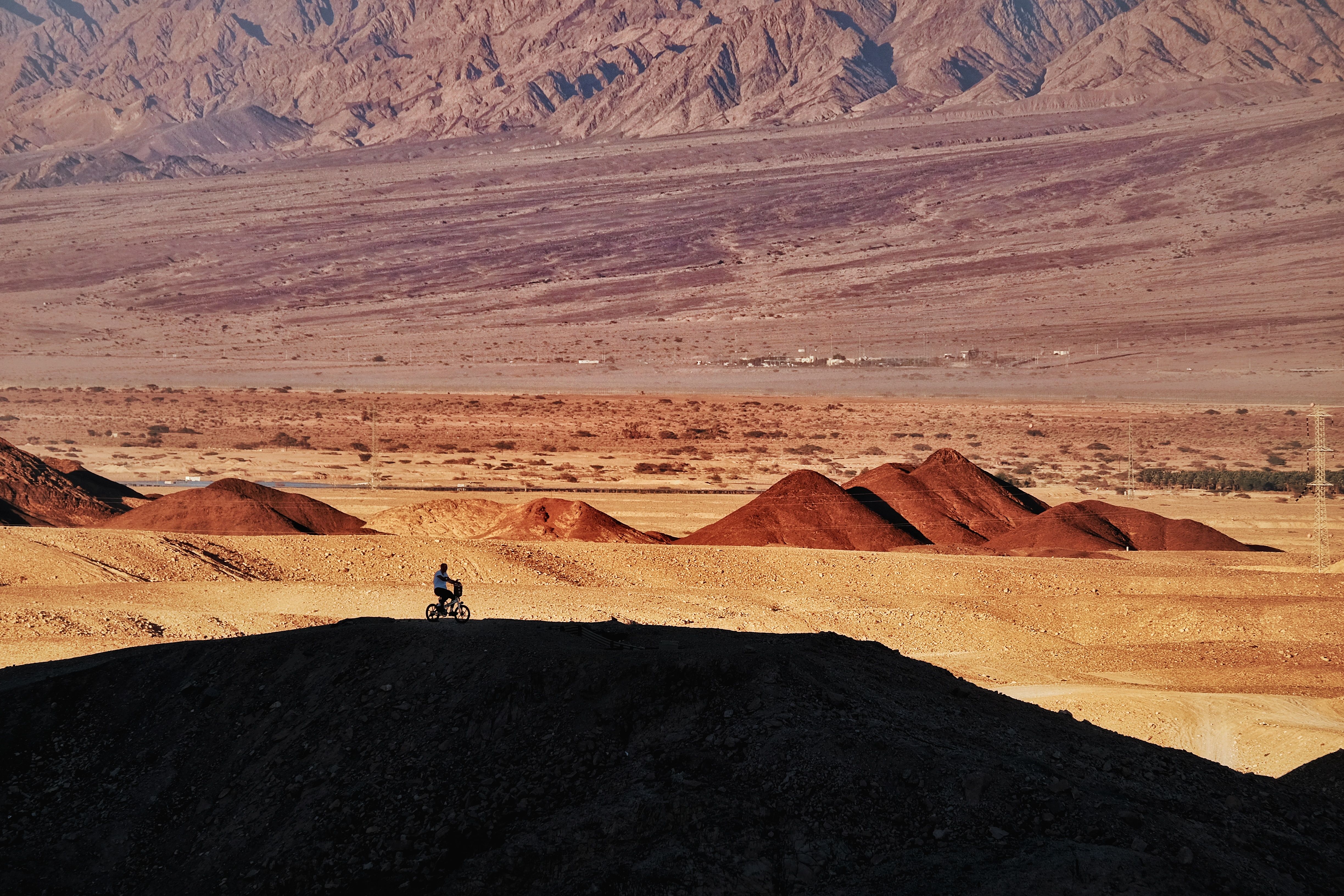 Lone cyclist riding along a dark ridge with red desert hills and rugged mountains beyond