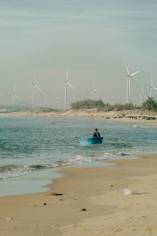 Free A peaceful beach scene with a lone boat and wind turbines in the background. Stock Photo