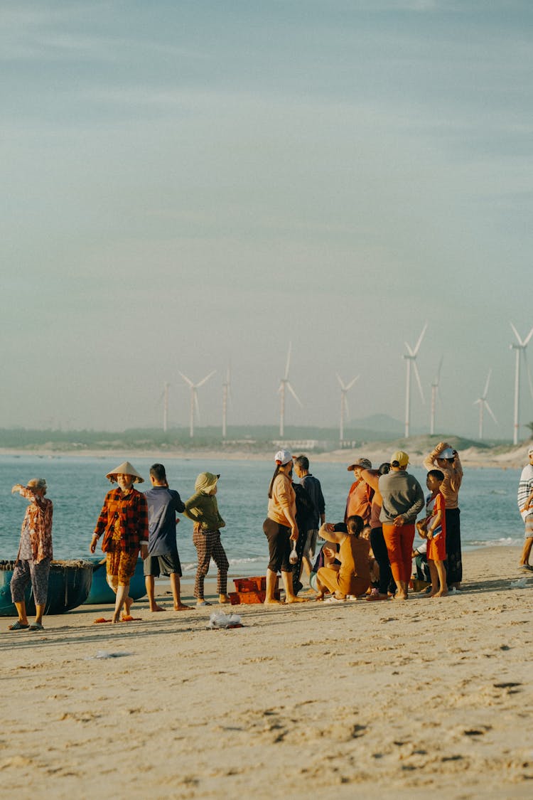 People On Sandy Beach Against Wind Turbines