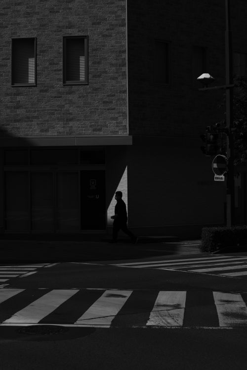 Free A silhouette of a man walking across an urban crosswalk, captured in high contrast black and white. Stock Photo