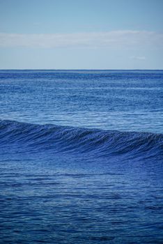 Peaceful ocean wave with a calm sea under a clear blue sky, perfect for serene nature themes.