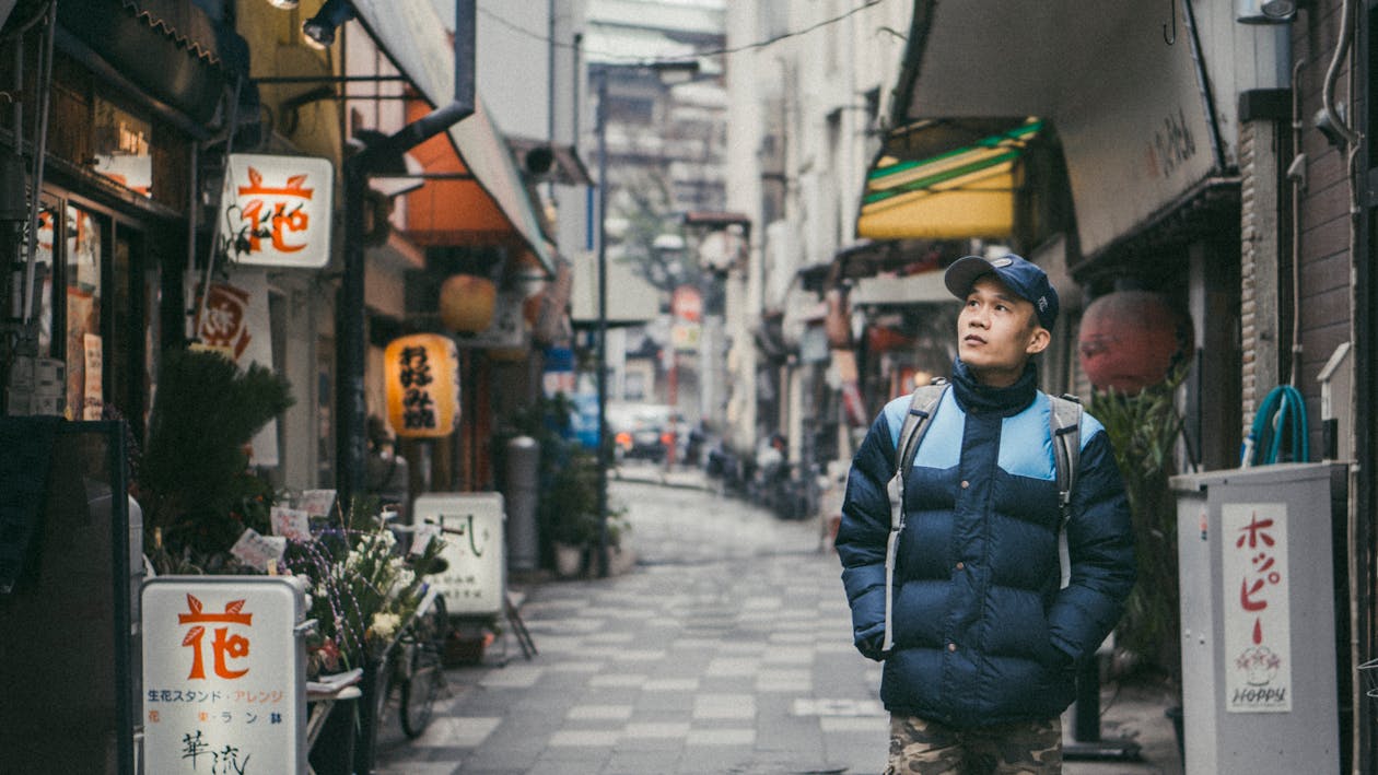 Man Walking on Grey Concrete Alley Surrounded by Buildings