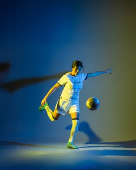 A female soccer player kicks a ball in a vibrant, dramatic studio setting.