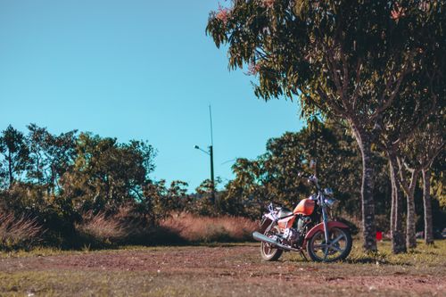 Free A vintage motorcycle parked amidst lush greenery under a clear blue sky, evoking a sense of adventure. Stock Photo