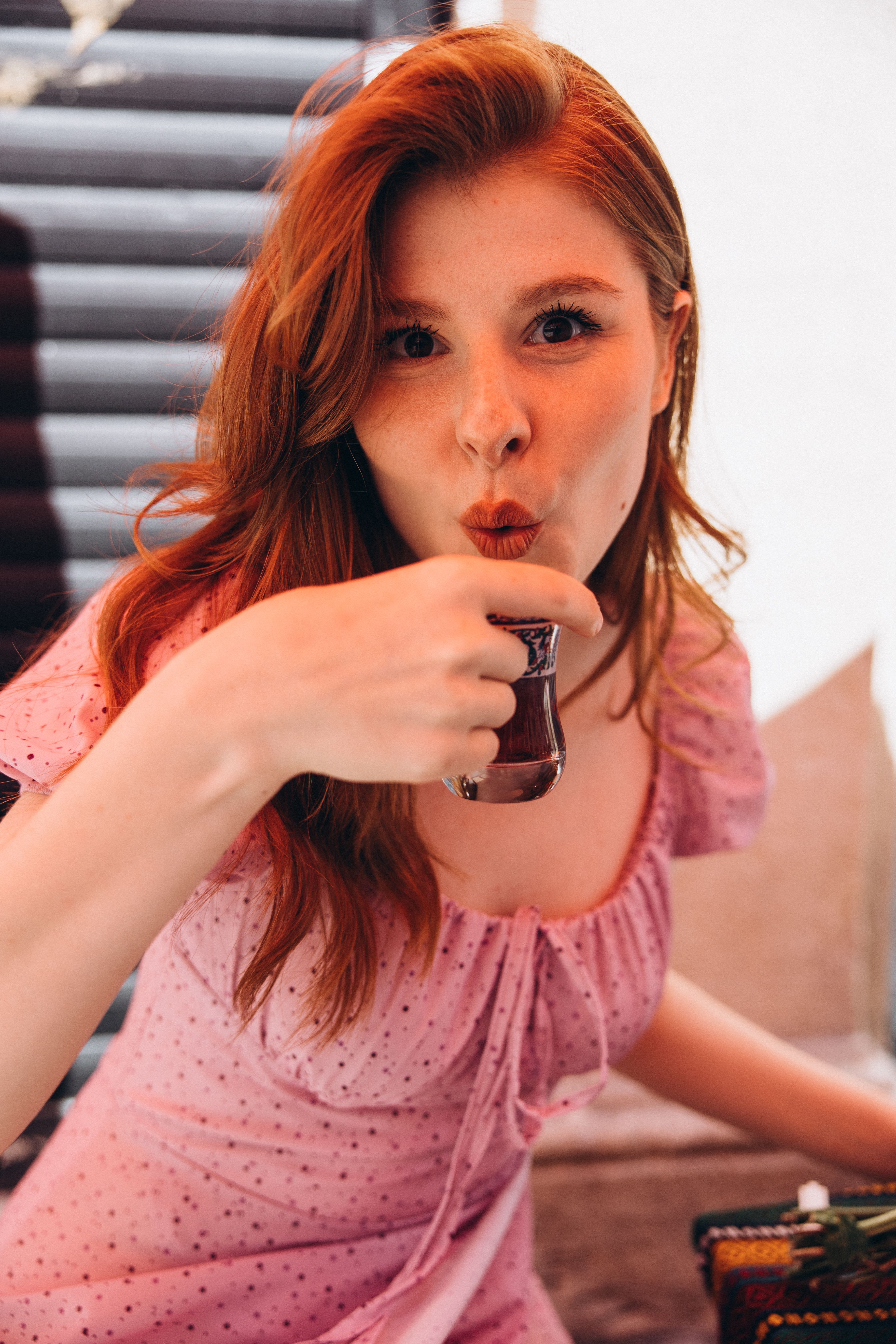 Young woman sipping traditional Turkish tea indoors with playful expression.
