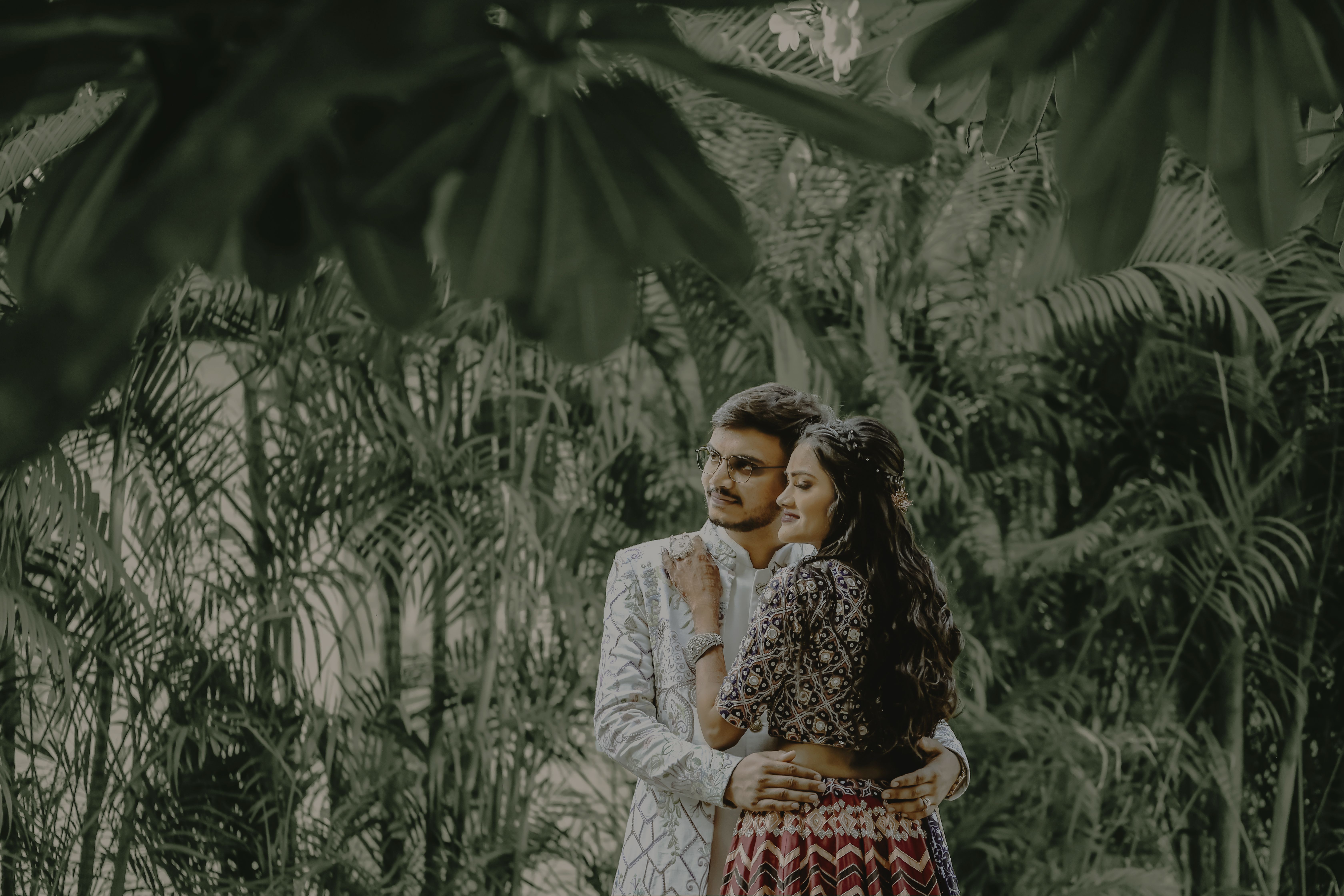 A loving couple in traditional clothing embracing amidst lush greenery.