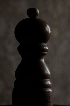 A close-up of a carved wooden pepper mill with a dark, moody background.