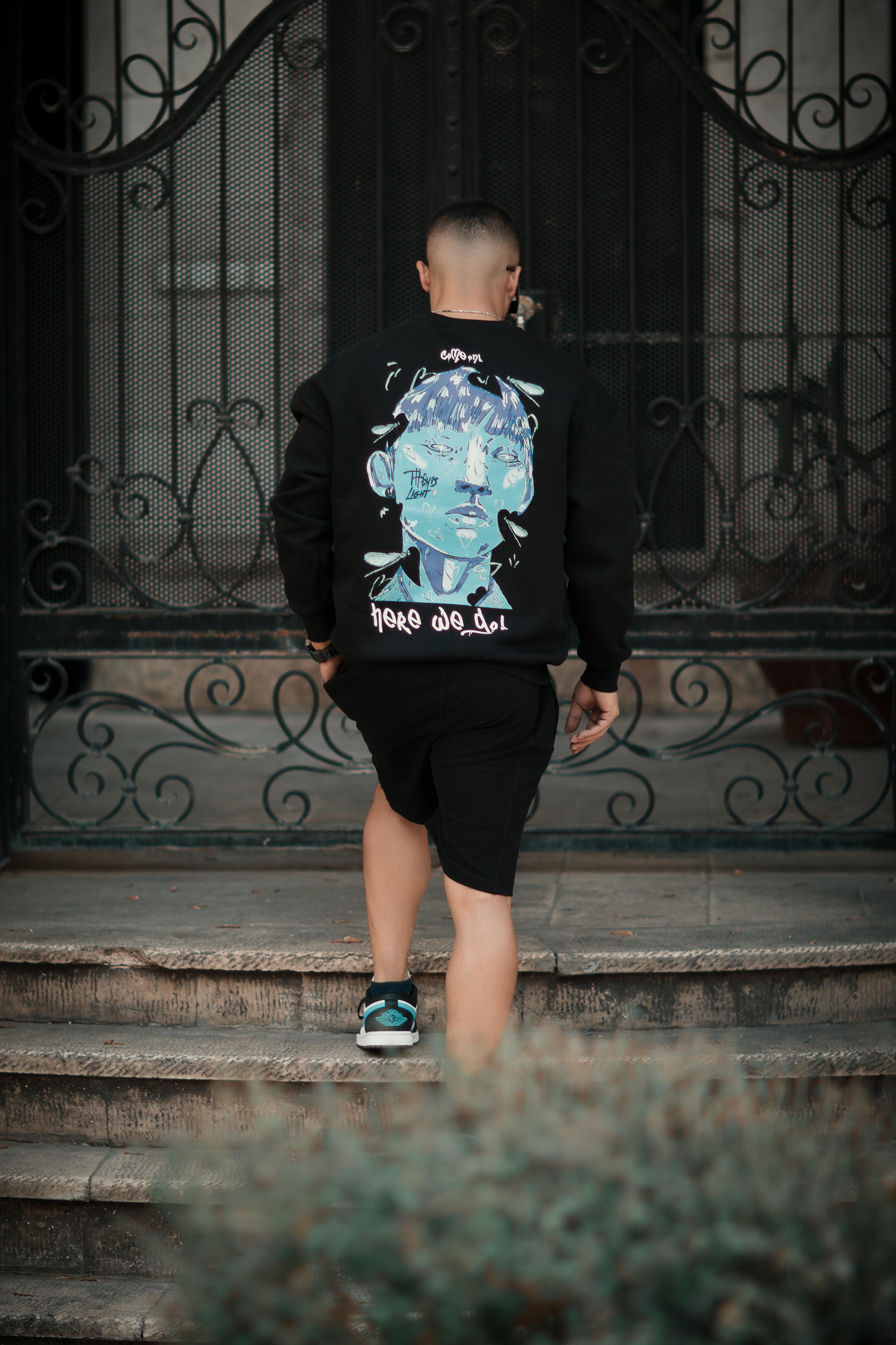 Young man showcasing street fashion in a graphic sweatshirt outdoors.