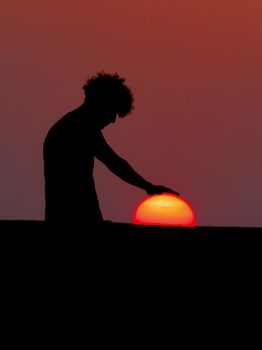 A dramatic silhouette of a man appearing to touch the setting sun at dusk.