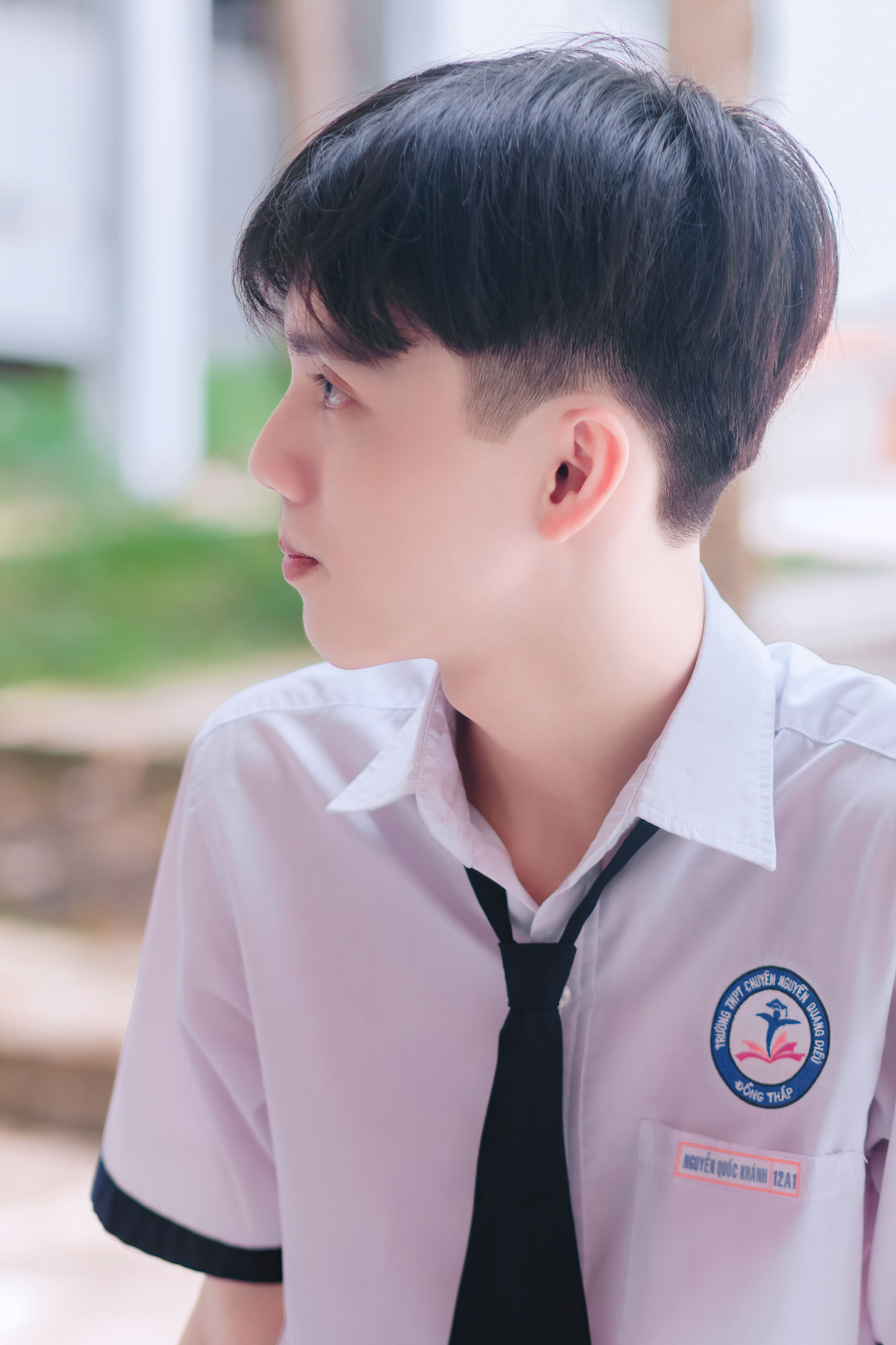 Side profile of an Asian student in a school uniform, outdoors.