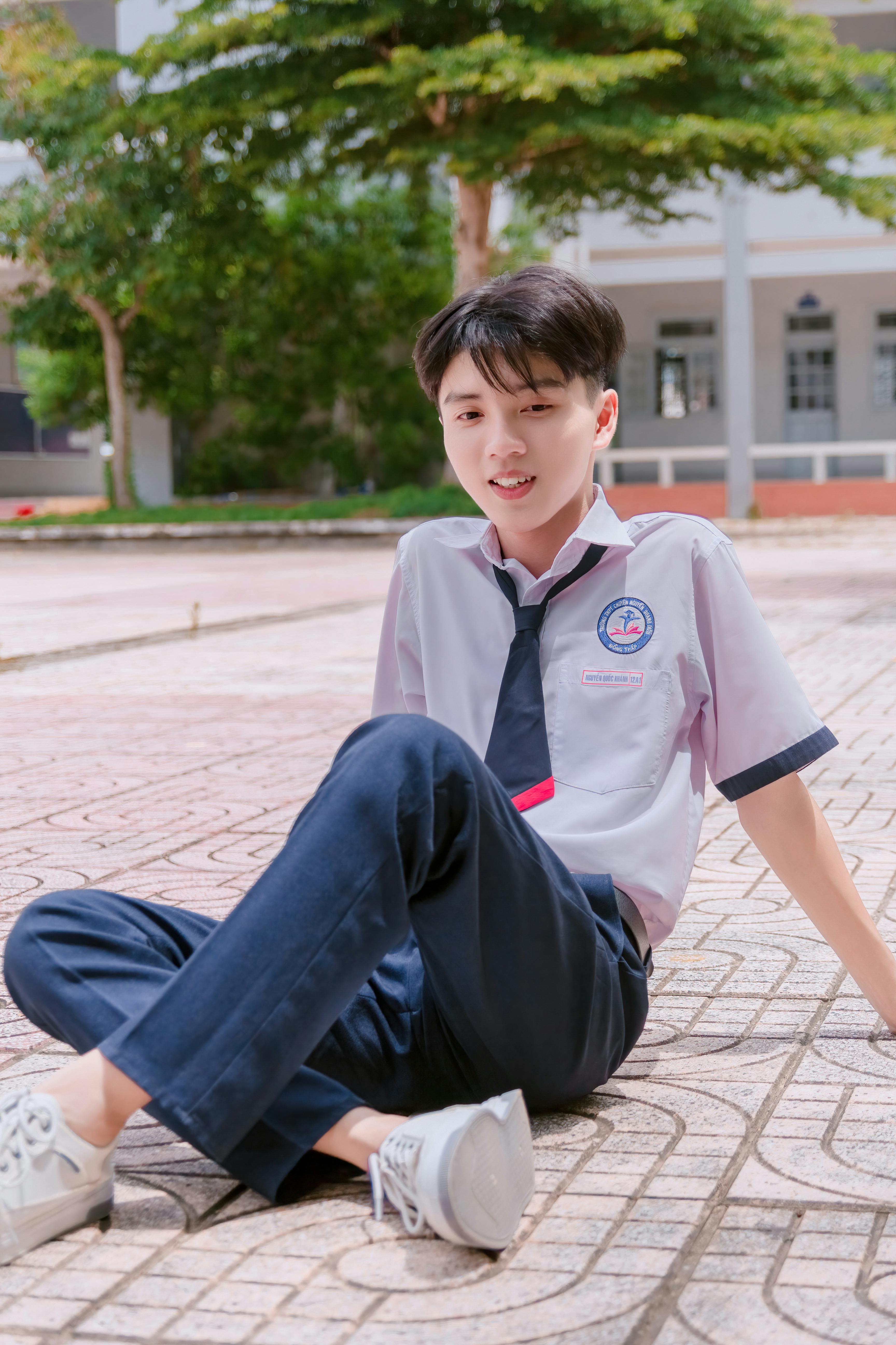 Portrait of a young Asian male student sitting cross-legged on a sunny campus day.