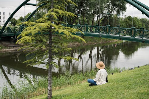 Woman with Hat Sitting on Grass Near River