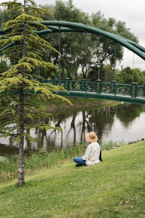 Woman with Hat Sitting on Grass by River