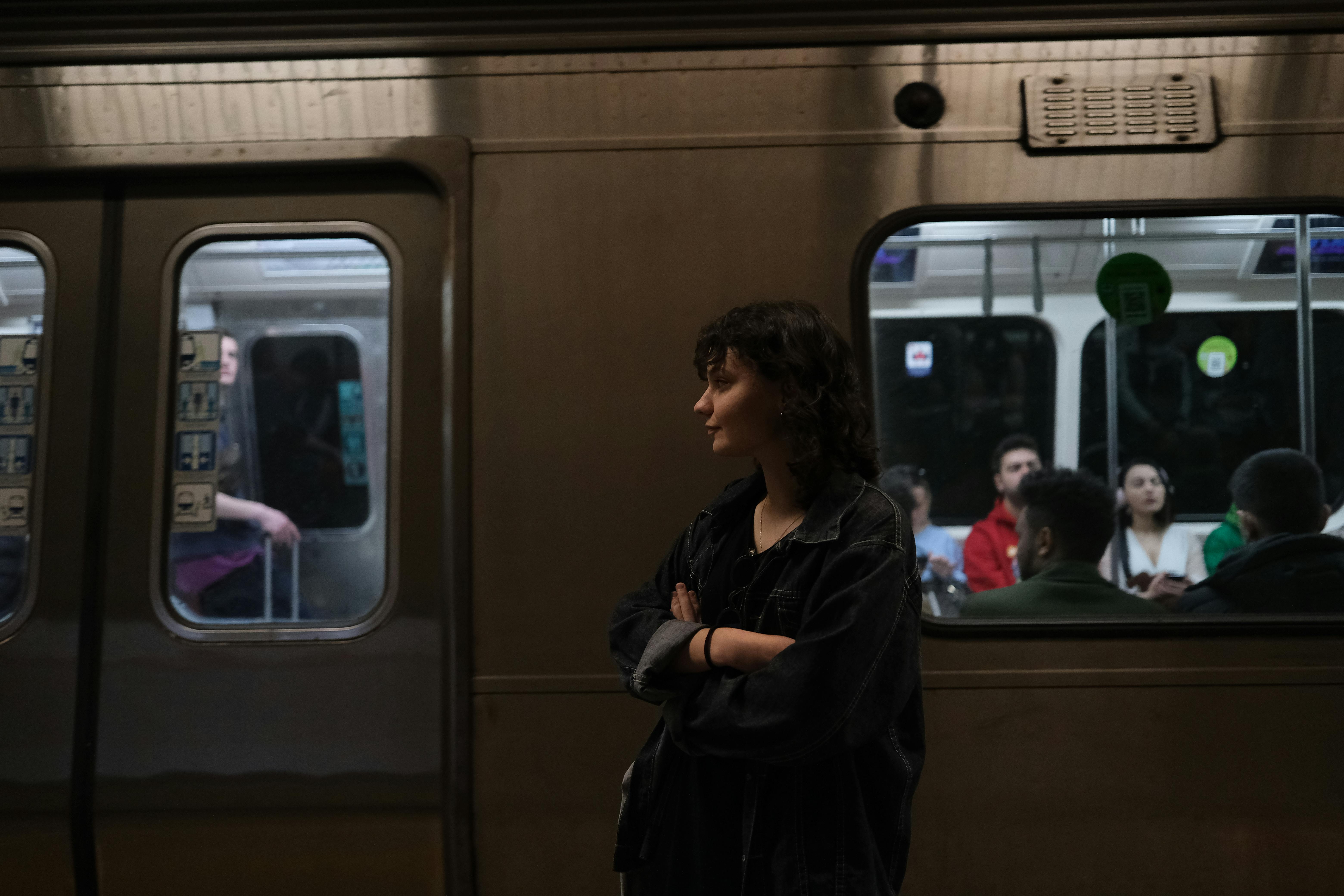 A woman waits at a subway station while passengers sit inside the train.