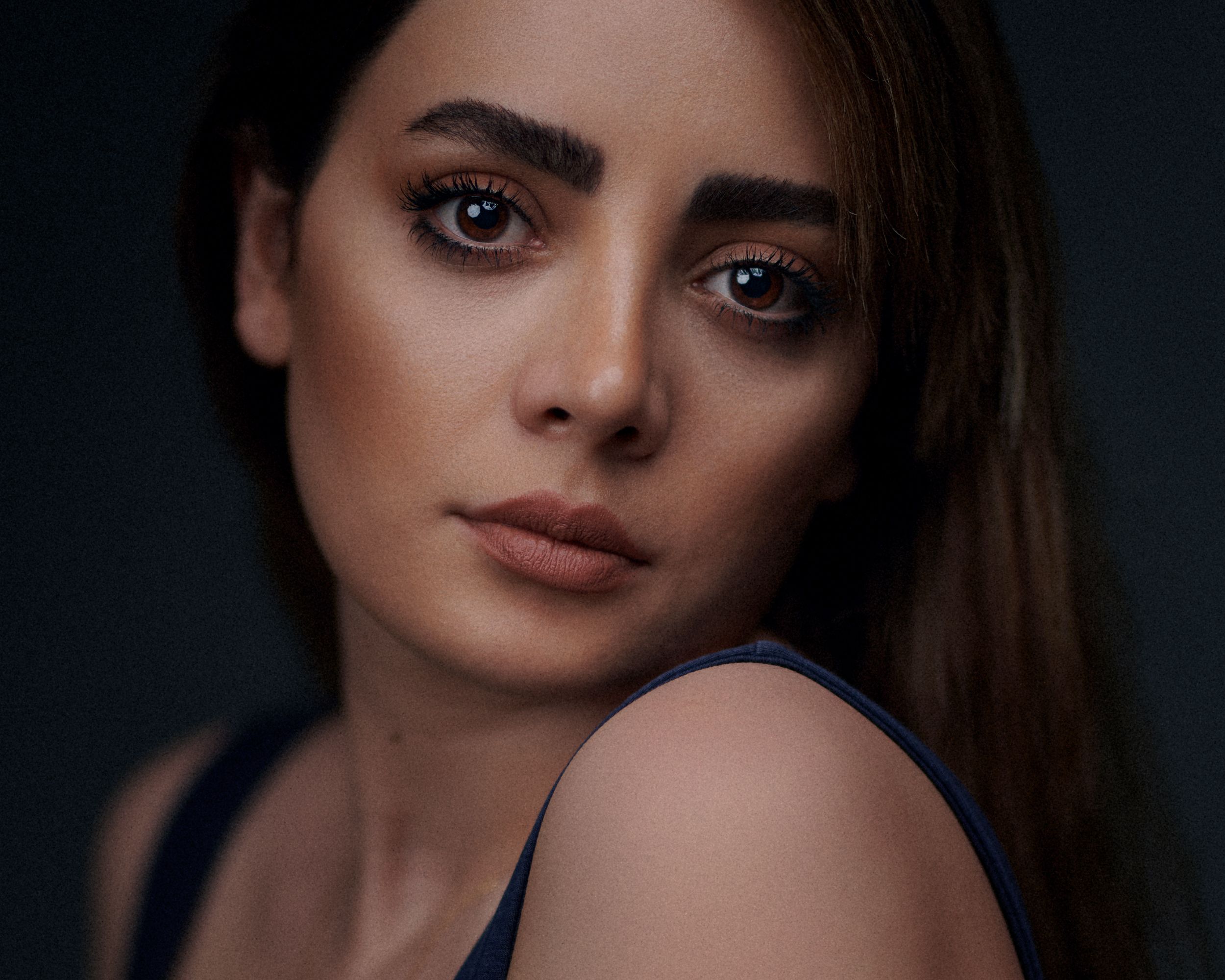 Close-up portrait of a woman with long hair and natural makeup against a dark background.