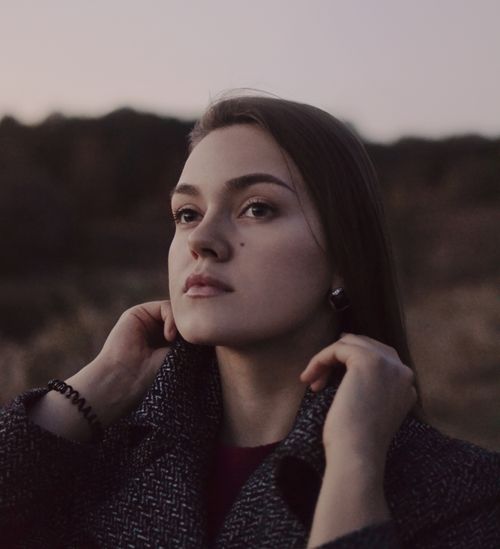 Free Outdoor portrait of a young woman adjusting her coat during dusk, showcasing natural beauty. Stock Photo