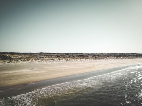A tranquil beach scene in Bindslev, Denmark, with calm waves and clear skies.