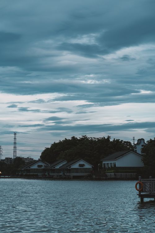 Free Tranquil riverside houses with overcast sky, evoking a serene evening atmosphere. Stock Photo