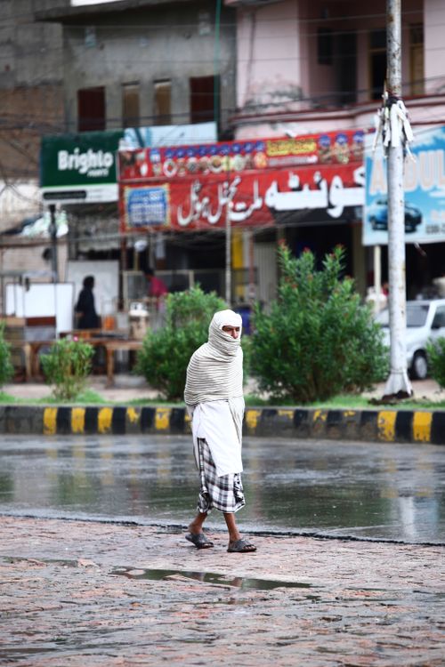 Free An individual walking on a wet city street after rainfall, surrounded by buildings. Stock Photo