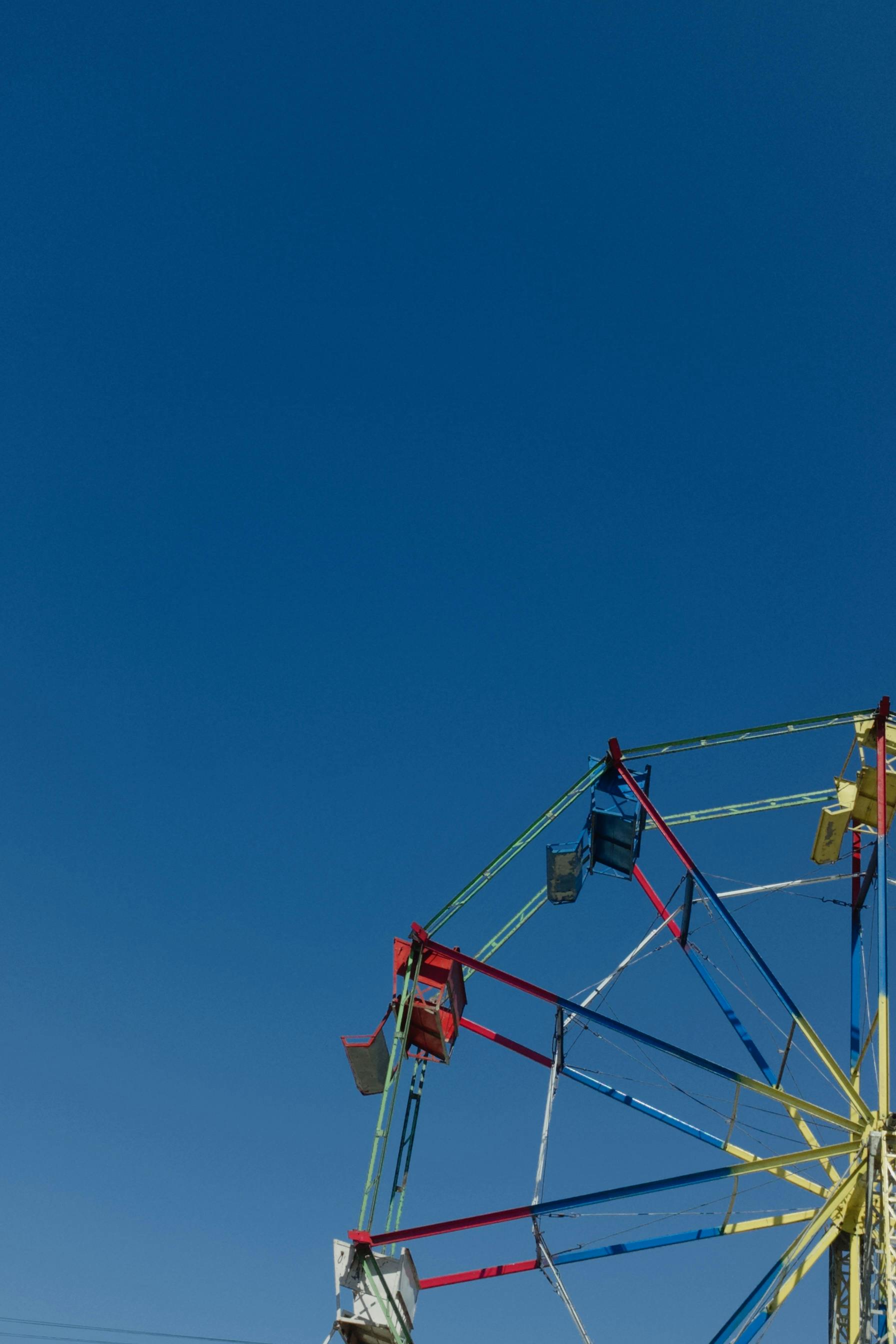 Bright Ferris wheel in a fairground setting under a clear blue sky. Ideal for summer themes.