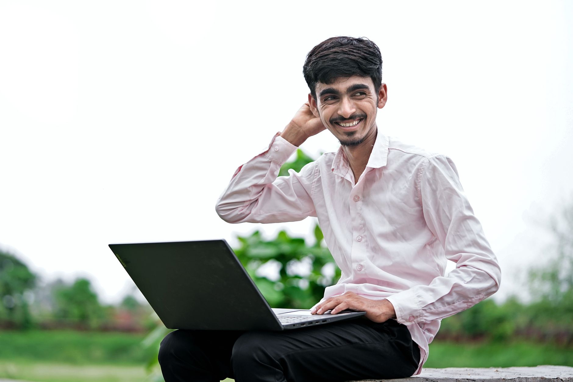 A cheerful young man poses with a laptop in a green outdoor setting. Perfect for tech and lifestyle themes.