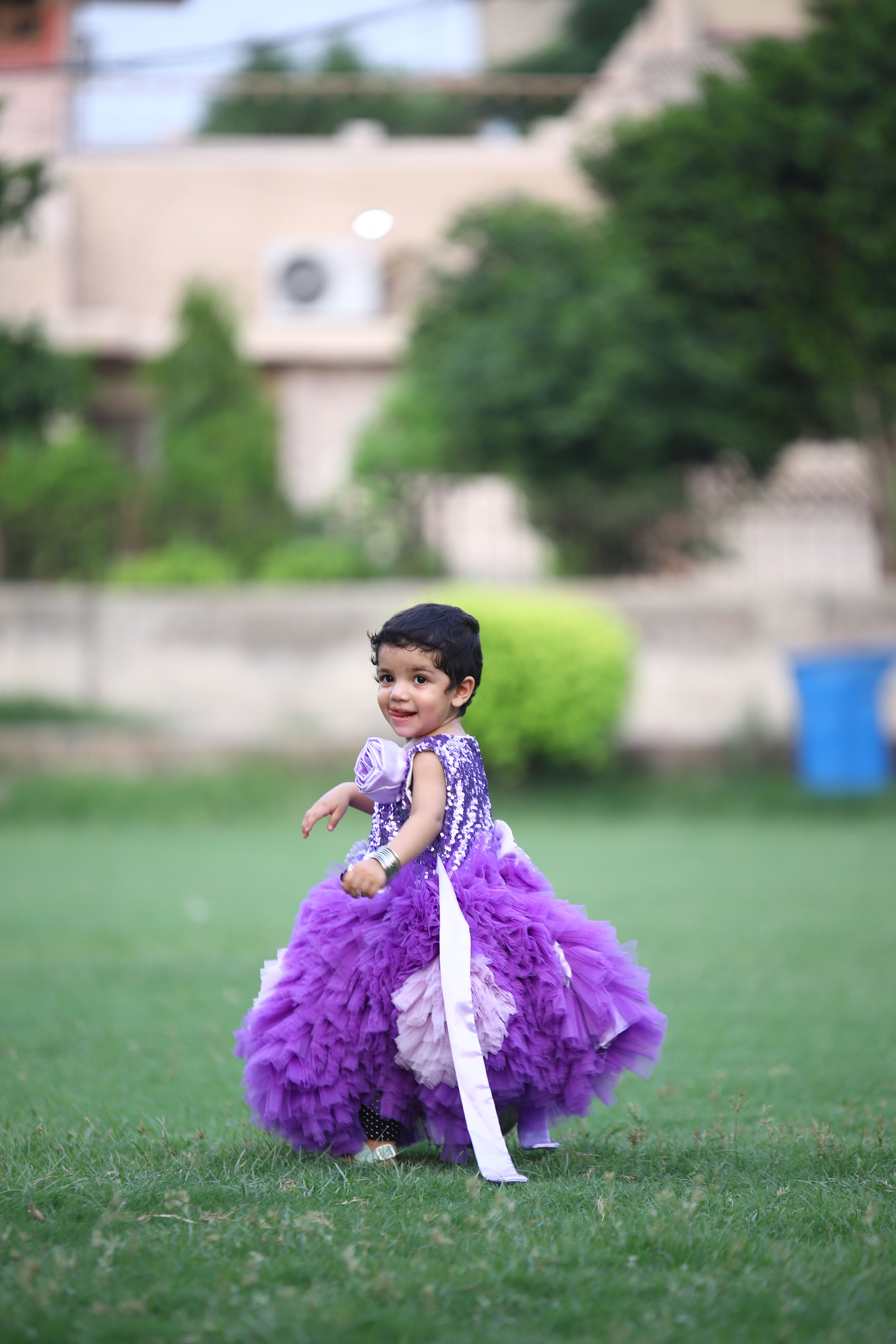 A cheerful child in a vibrant purple dress enjoys a playful moment on a sunny day.