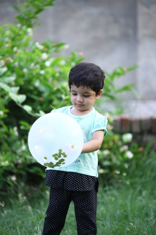 Free A young girl plays with a balloon in a lush green garden under the summer sun. Stock Photo