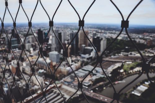 Free Blurred city skyline view through a chain link fence, creating a sense of depth. Stock Photo