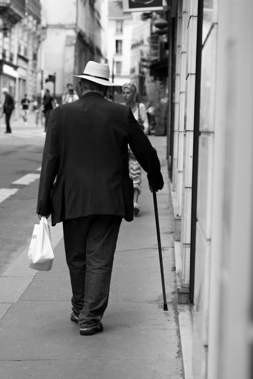 Free Elderly man in elegant attire with a walking stick strolling through a city sidewalk. Stock Photo