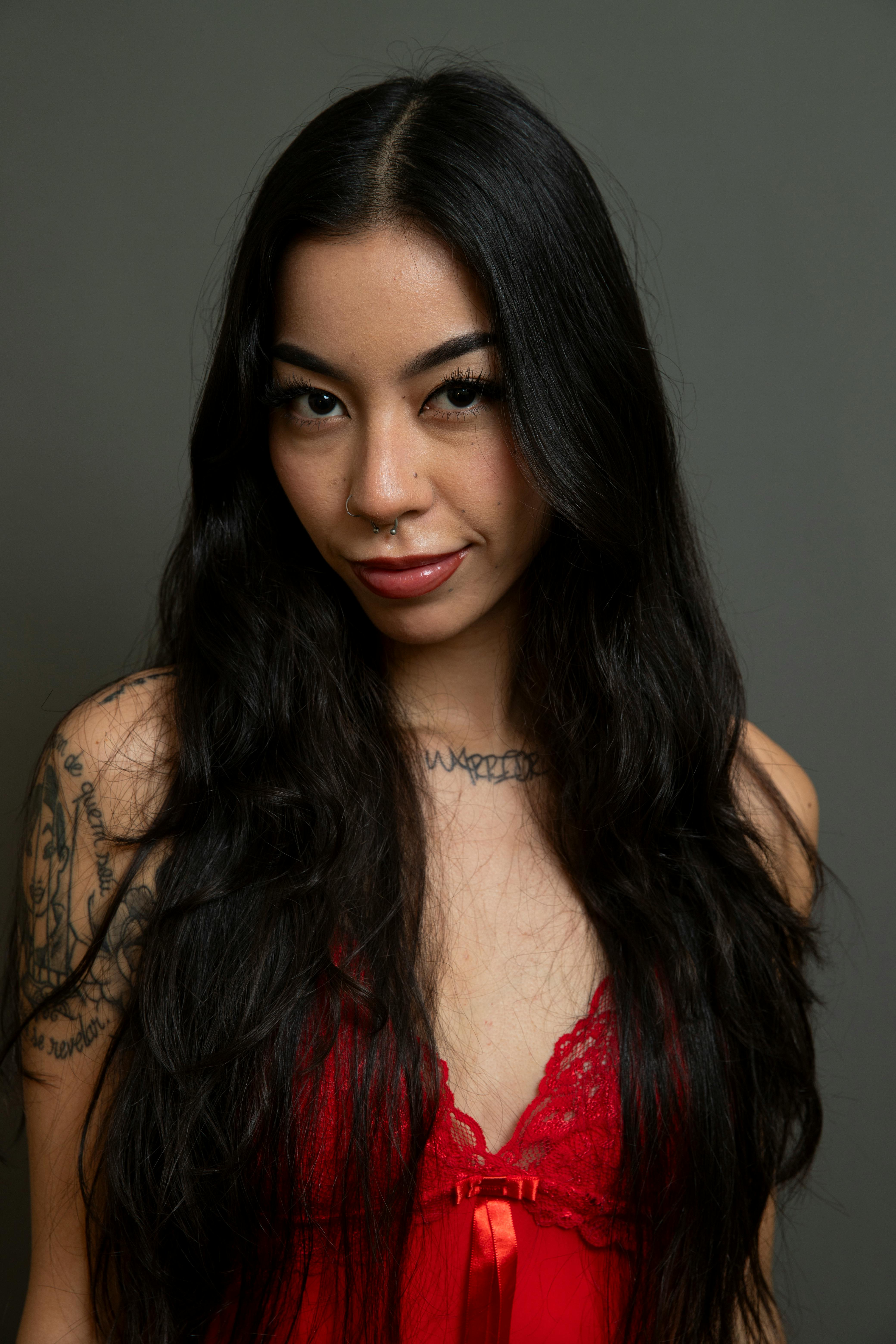 Striking portrait of a confident woman with tattoos in a red outfit against a gray background.
