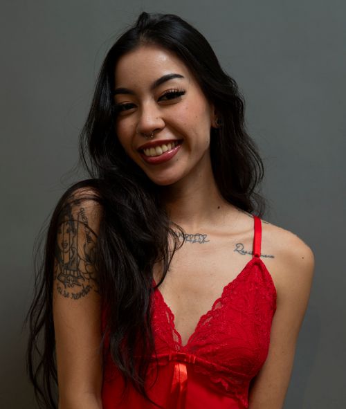 Free Portrait of a smiling woman with long hair and tattoos in a red dress against a gray background. Stock Photo