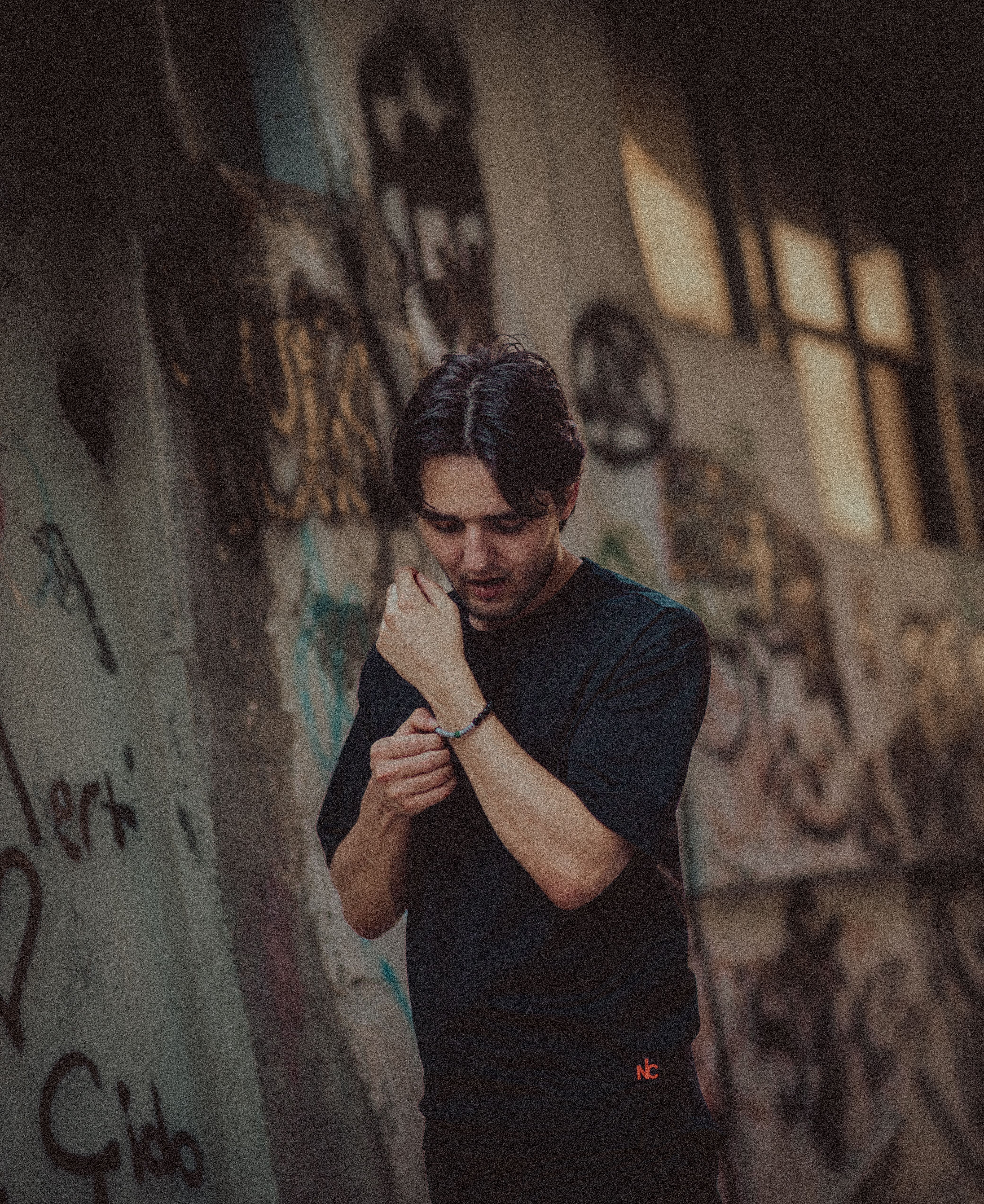 A young man in casual attire stands near a graffiti-covered wall, creating an urban vibe.