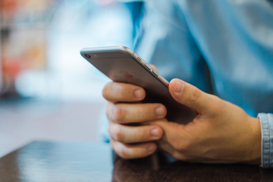 A person holding a smartphone with a cracked screen that says 'FAKE NEWS', representing media distrust.