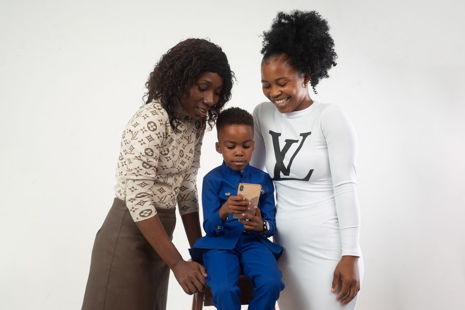Happy family moment with a child using a smartphone surrounded by loving adults.