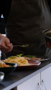 Chef prepares pasta with fresh herbs and garnish in modern kitchen setting.