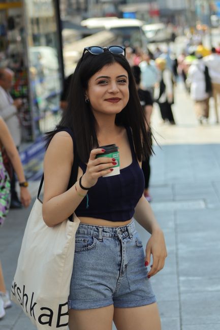 Smiling woman in summer street fashion enjoying coffee outdoors.