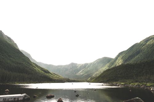 Free Tranquil view of a lake surrounded by lush green mountains under bright sky. Stock Photo