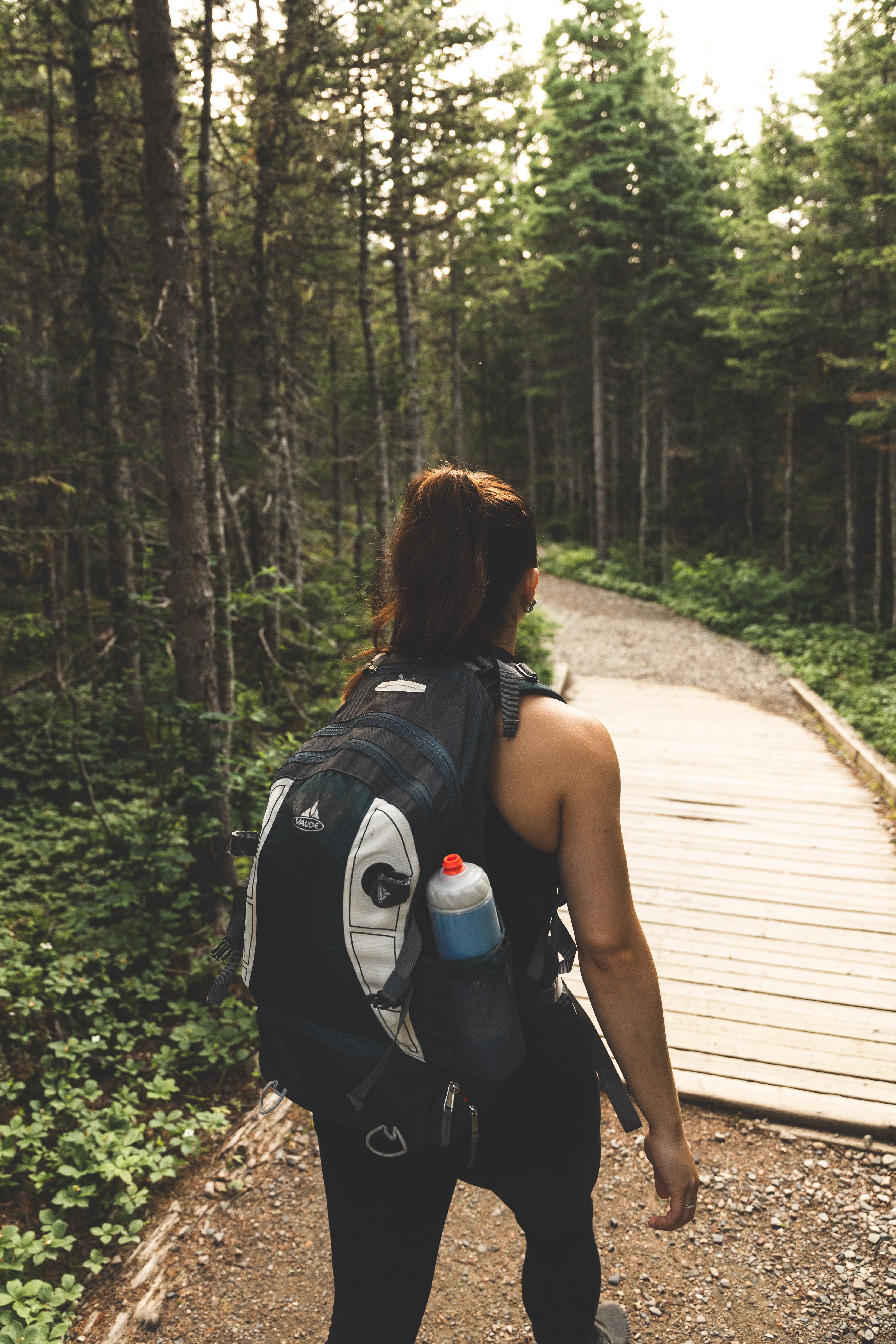 Woman walking a forest trail with a loaded backpack and water bottle