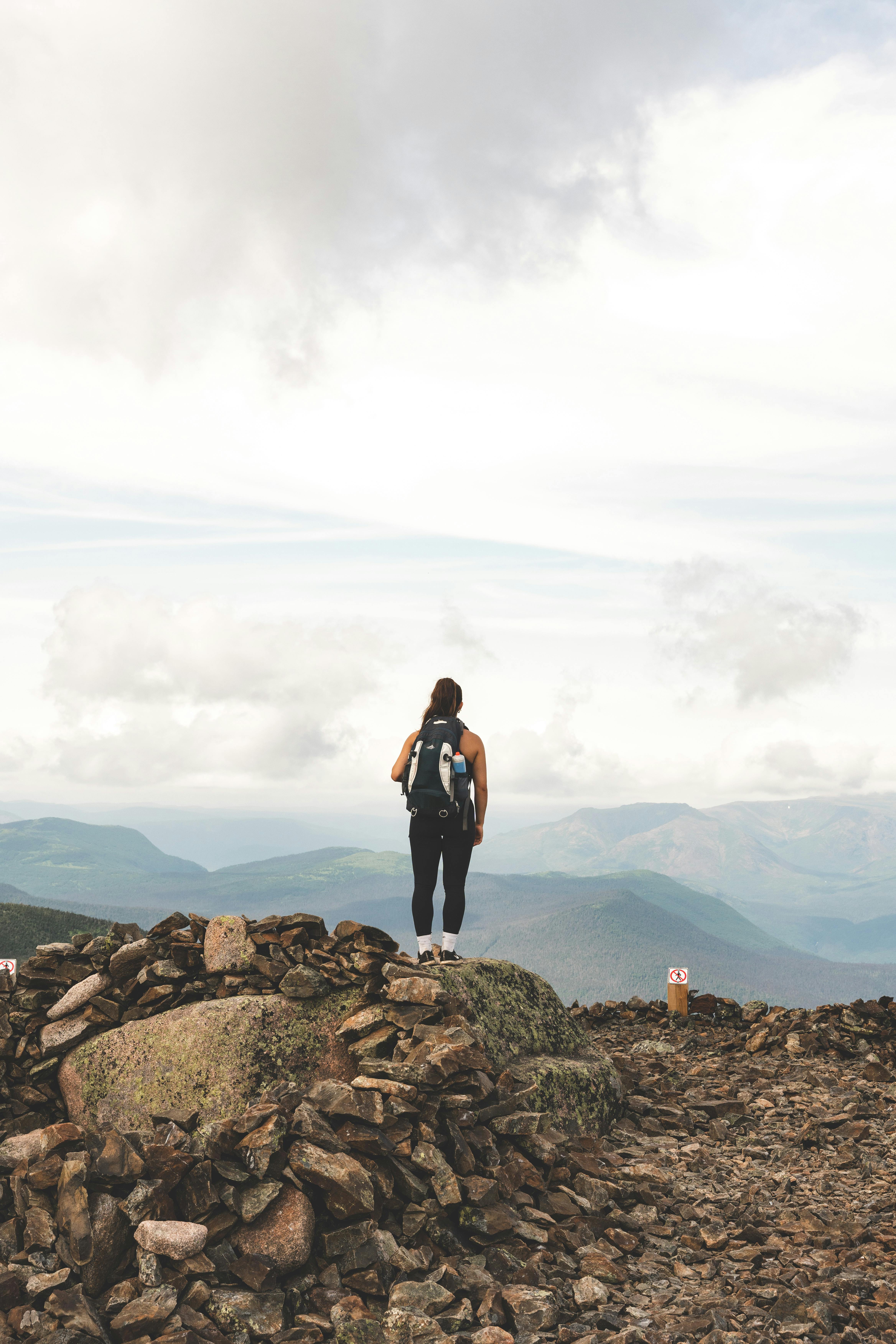 A hiker stands alone on rocky terrain, gazing at the expansive mountain view.