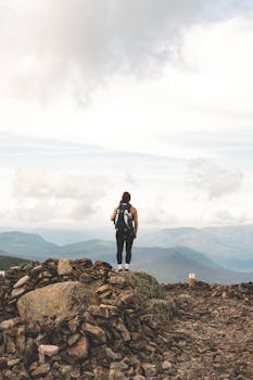 A hiker stands alone on rocky terrain, gazing at the expansive mountain view.