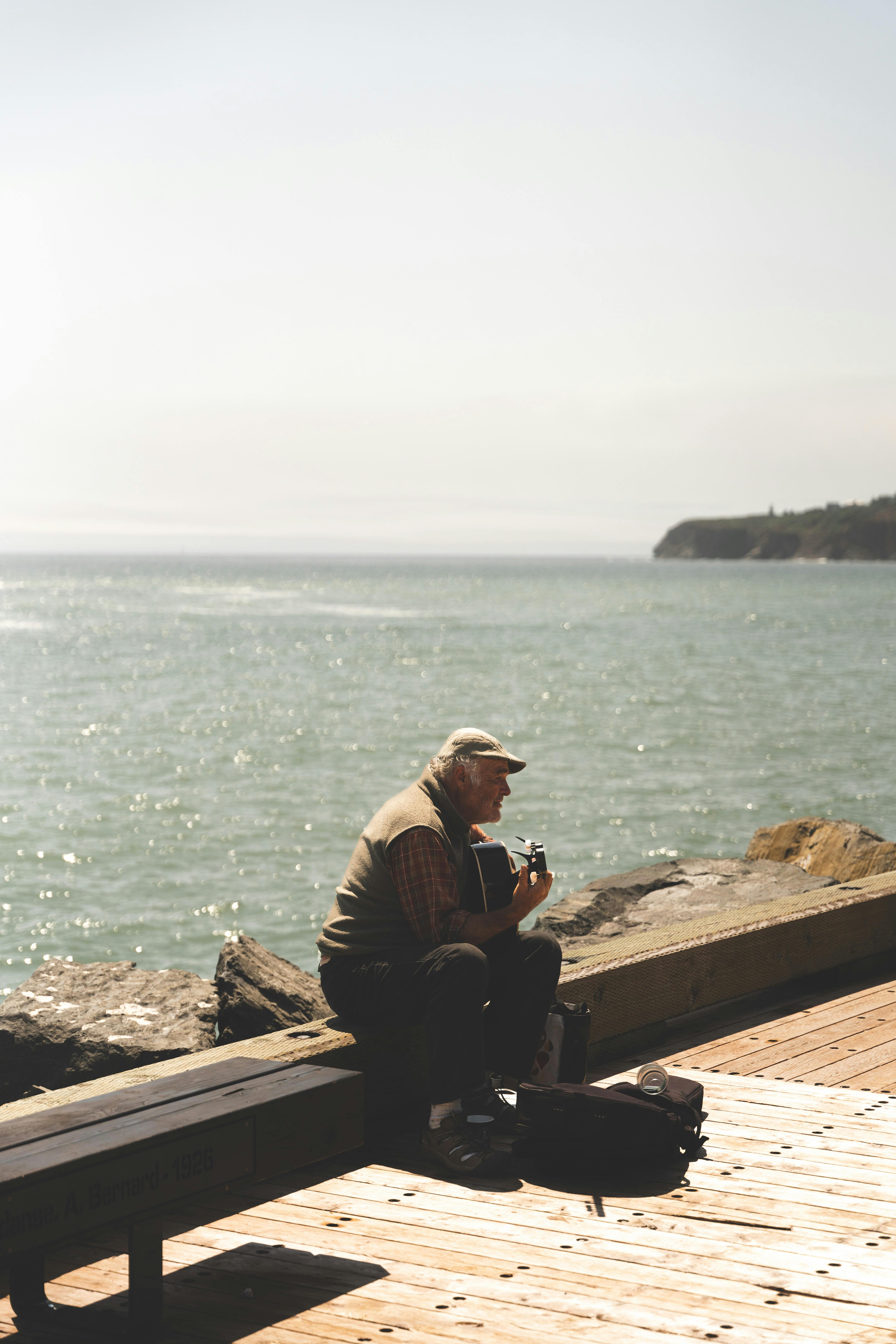 an older man sitting on a dock looking at the ocean