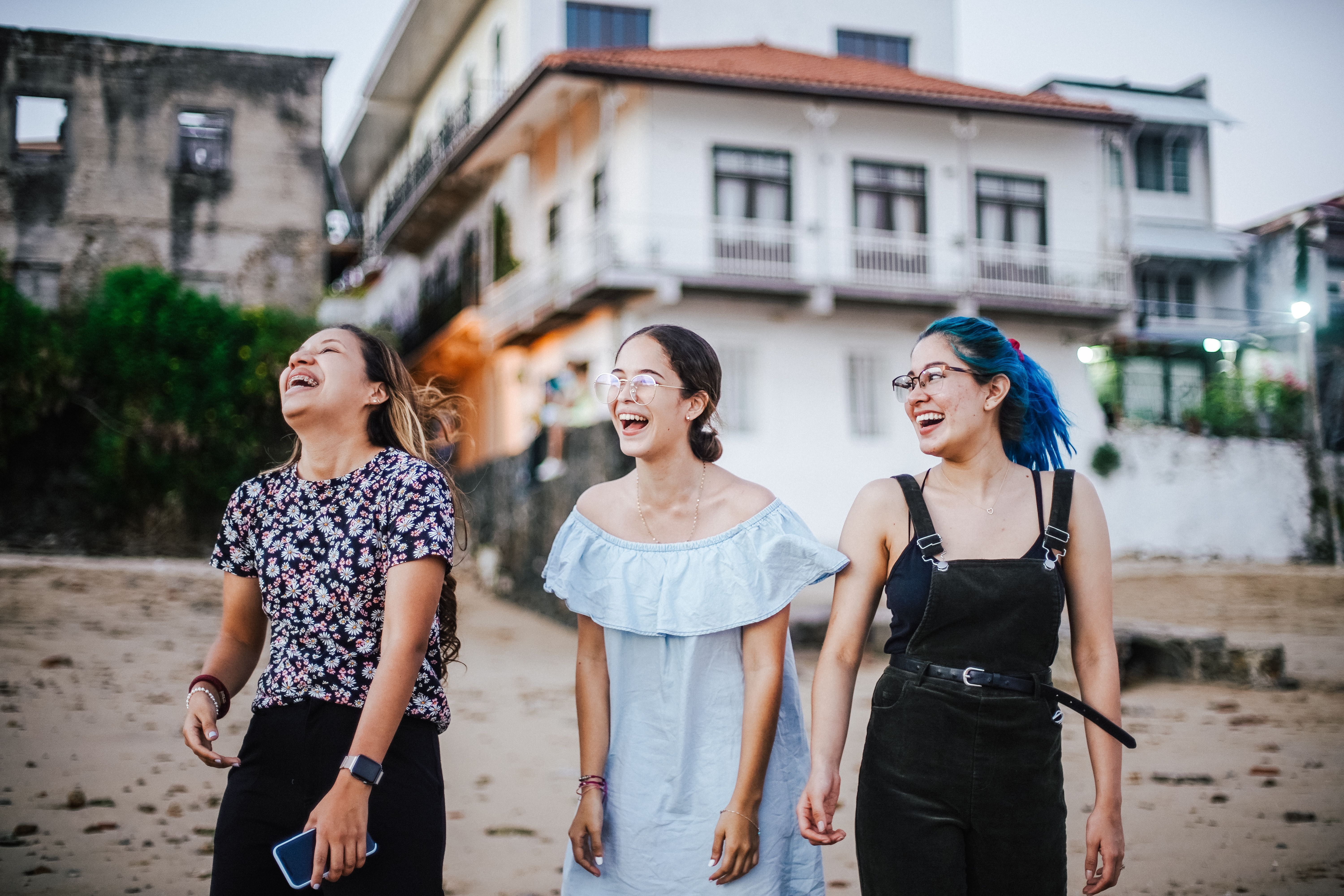 Three young women enjoying laughter and friendship by a beachfront building.